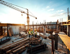 Construction industry concept - architects and engineers discussing work progress between concrete walls, scaffolds and cranes.