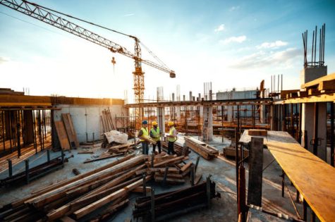 Construction industry concept - architects and engineers discussing work progress between concrete walls, scaffolds and cranes.